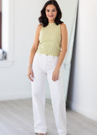 Woman wearing a light green sleeveless top and white pants indoors.