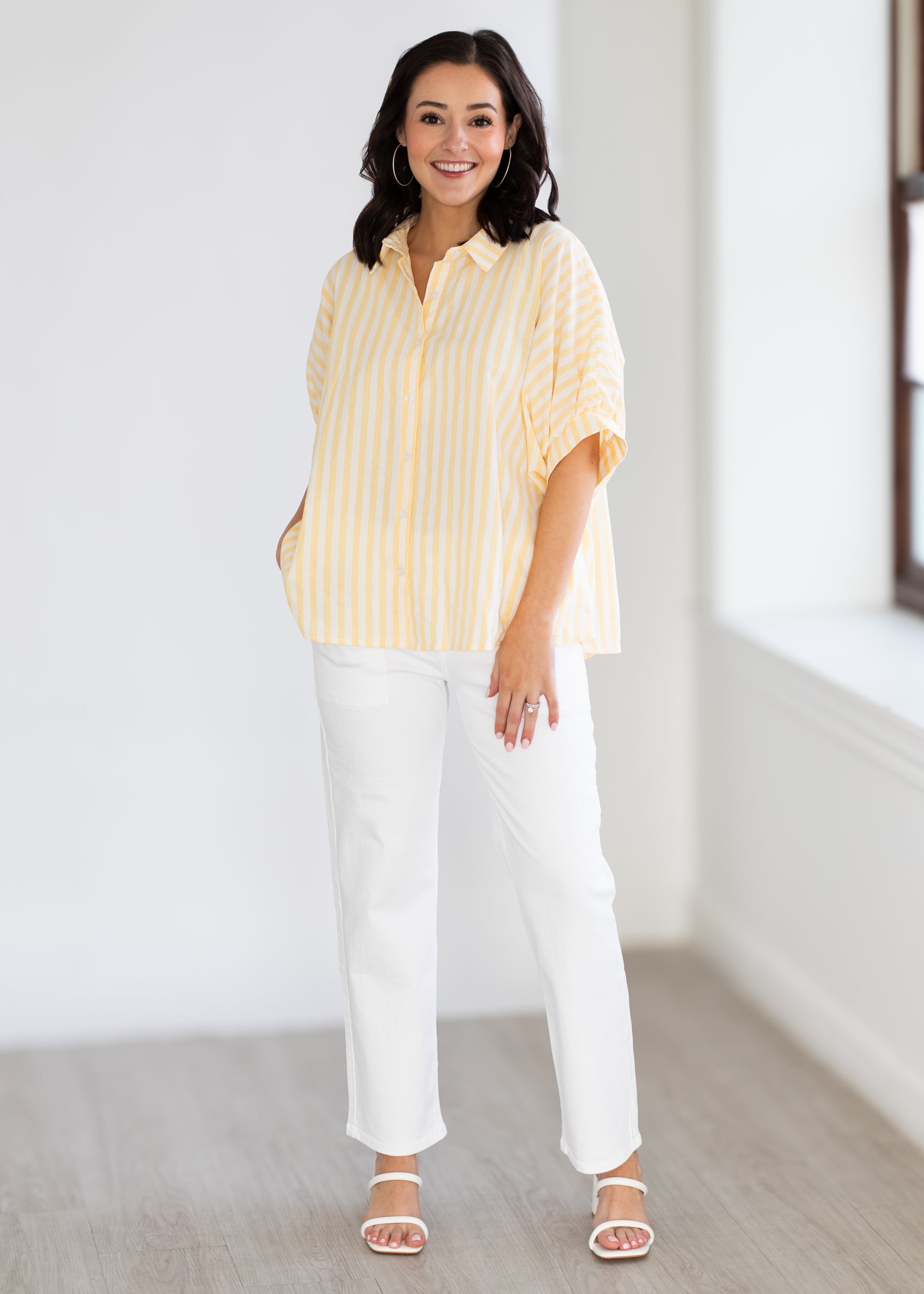 Woman wearing a yellow striped shirt and white pants in a minimal indoor setting