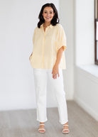 Woman wearing a yellow striped shirt and white pants in a minimal indoor setting