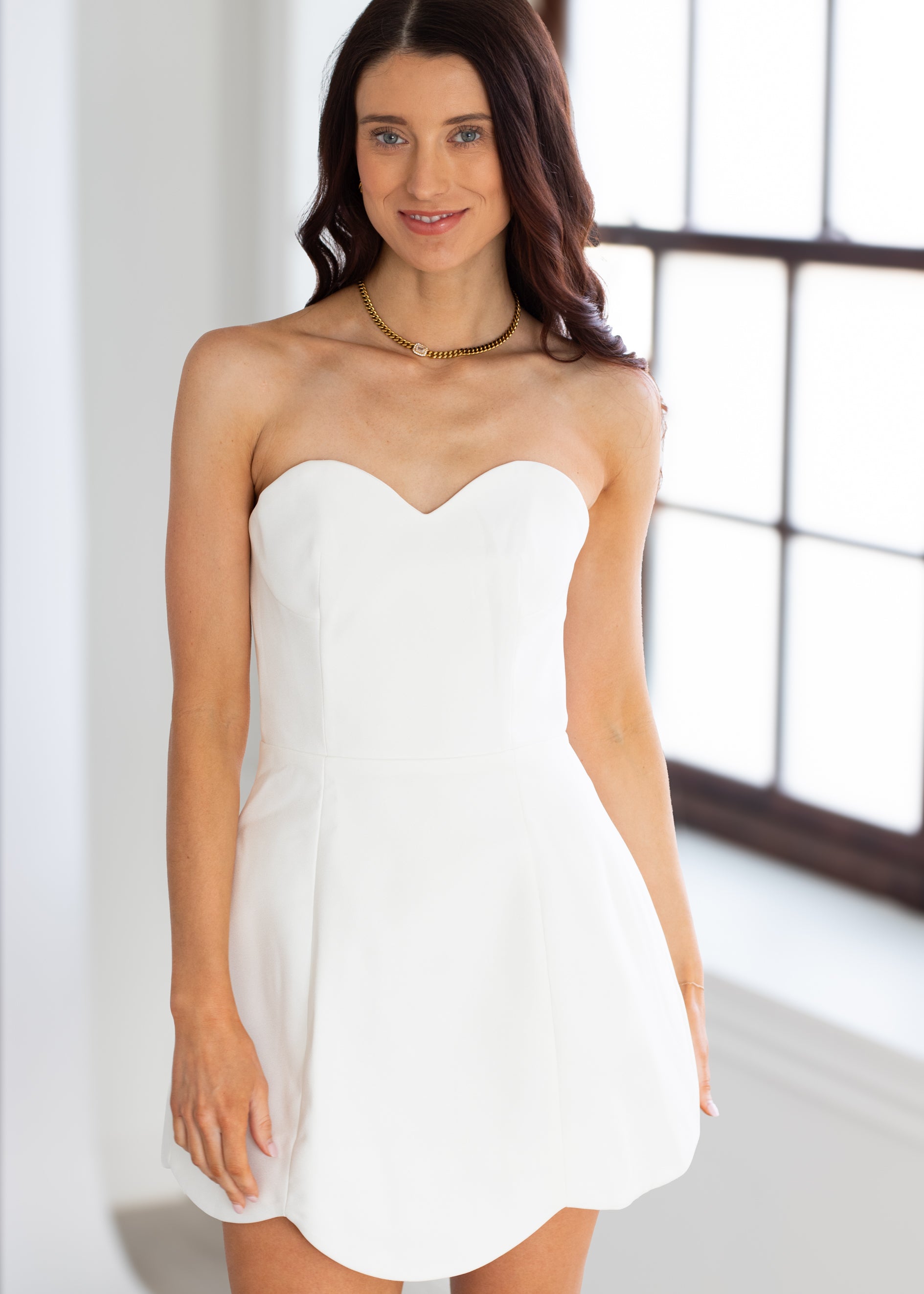 Woman wearing a strapless white dress indoors with a neutral background