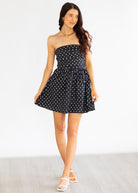 Woman wearing a black strapless dress with white polka dots on a plain background
