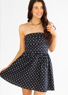 Woman wearing a black strapless dress with white polka dots on a white background