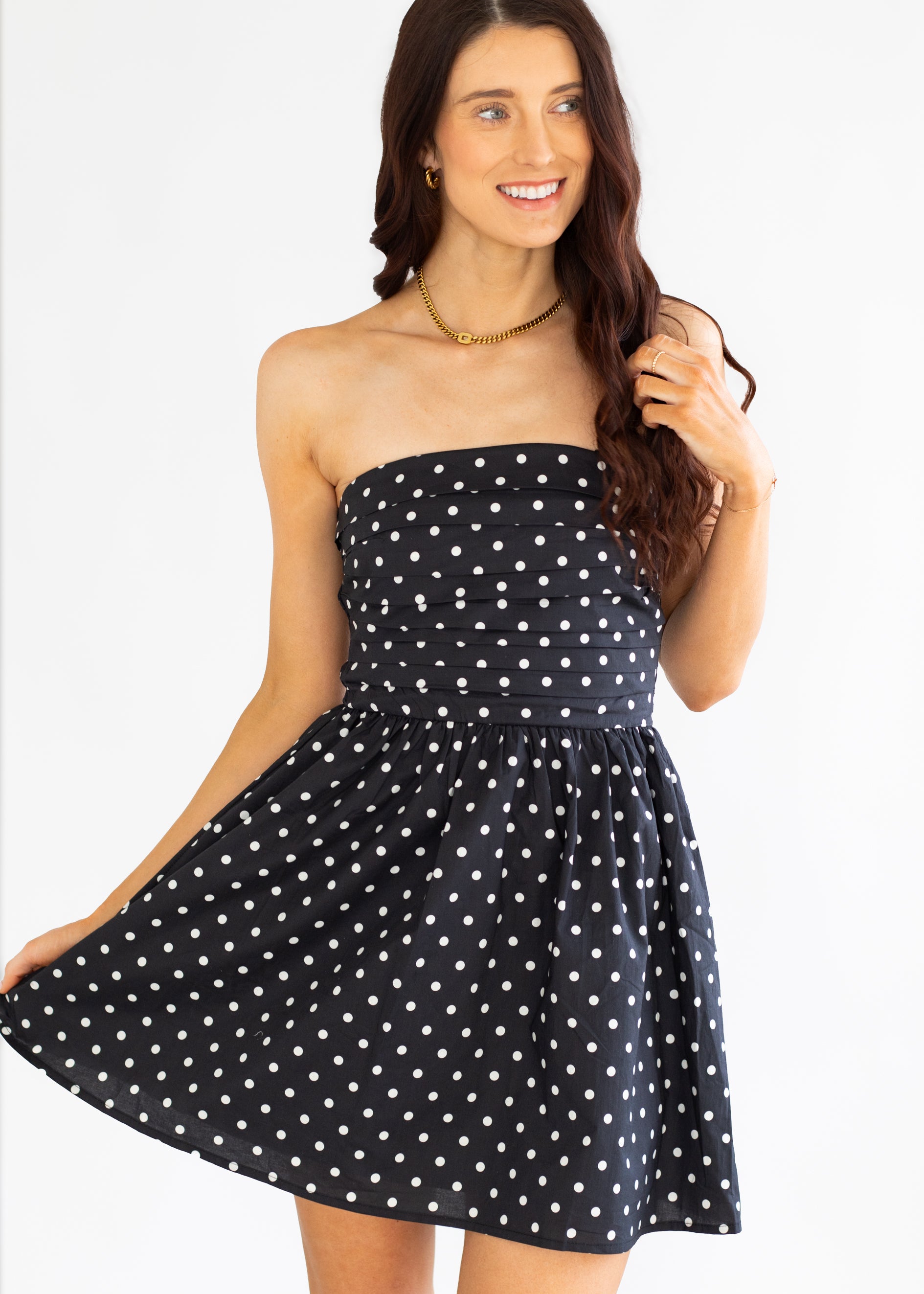 Woman wearing a black strapless dress with white polka dots on a white background