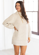 Woman wearing a beige ribbed sweater dress in a bright room.