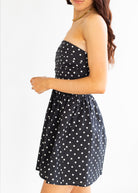 Woman wearing a black strapless dress with white polka dots on a white background