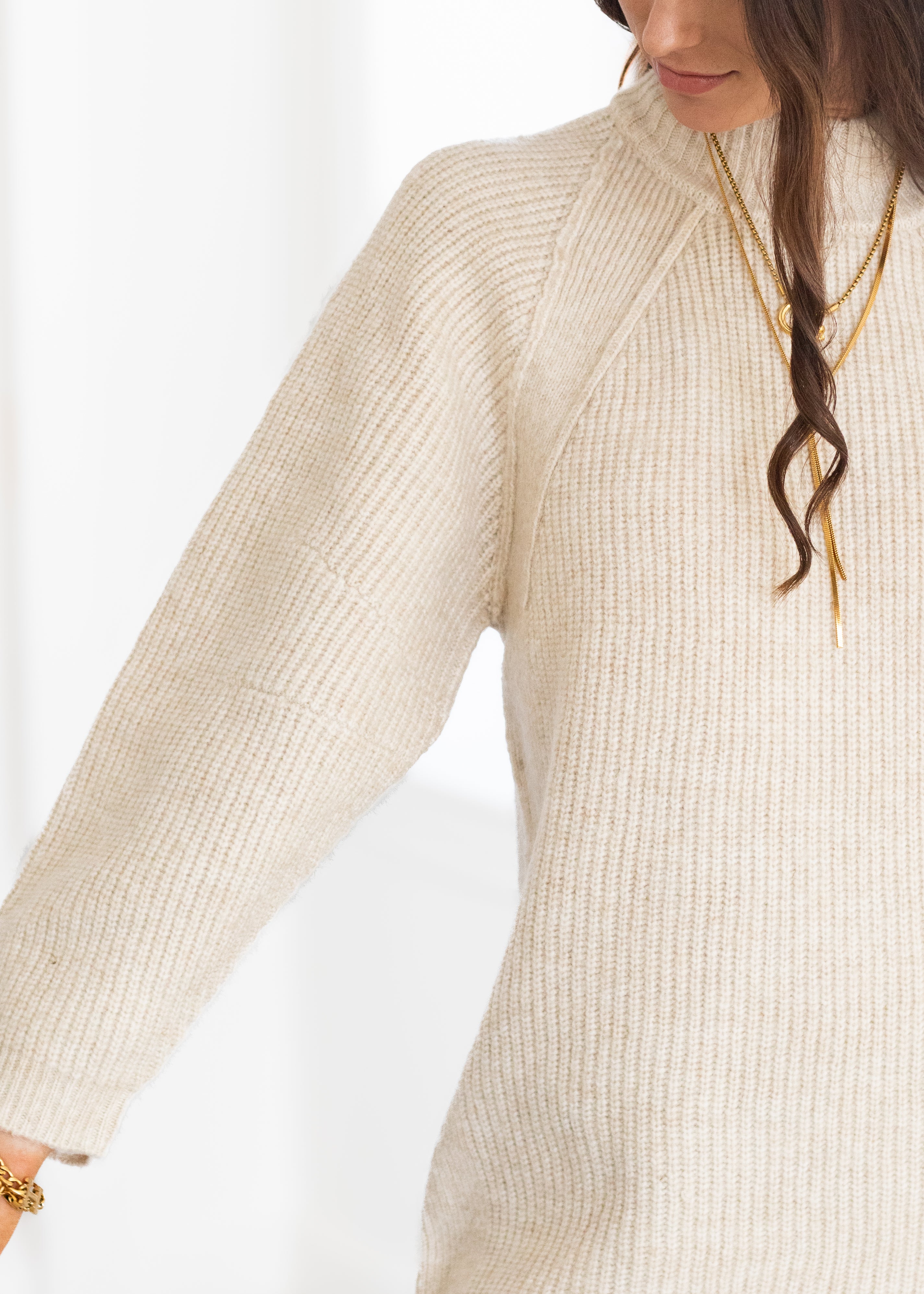 Close-up of a person wearing a beige ribbed sweater on a white background