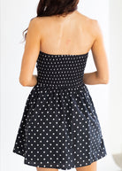 Black strapless dress with white polka dots on a plain background