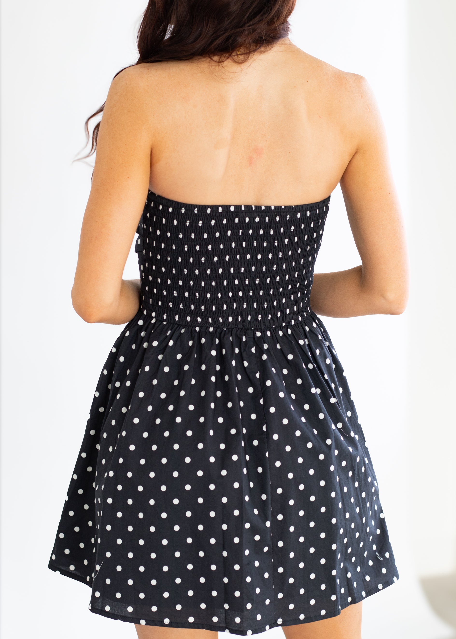 Black strapless dress with white polka dots on a plain background