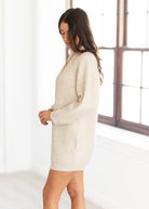 Woman wearing a beige sweater dress in a bright room.