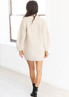 Person wearing a cream-colored sweater dress in a minimalistic setting