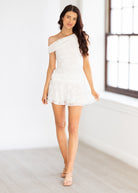 Woman wearing a white off-shoulder dress in a bright room.