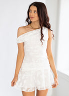 Woman wearing a white one-shoulder dress against a plain background