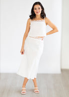 Woman wearing a white outfit with a lace top and skirt against a plain background