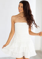 Woman wearing a white strapless dress against a plain background
