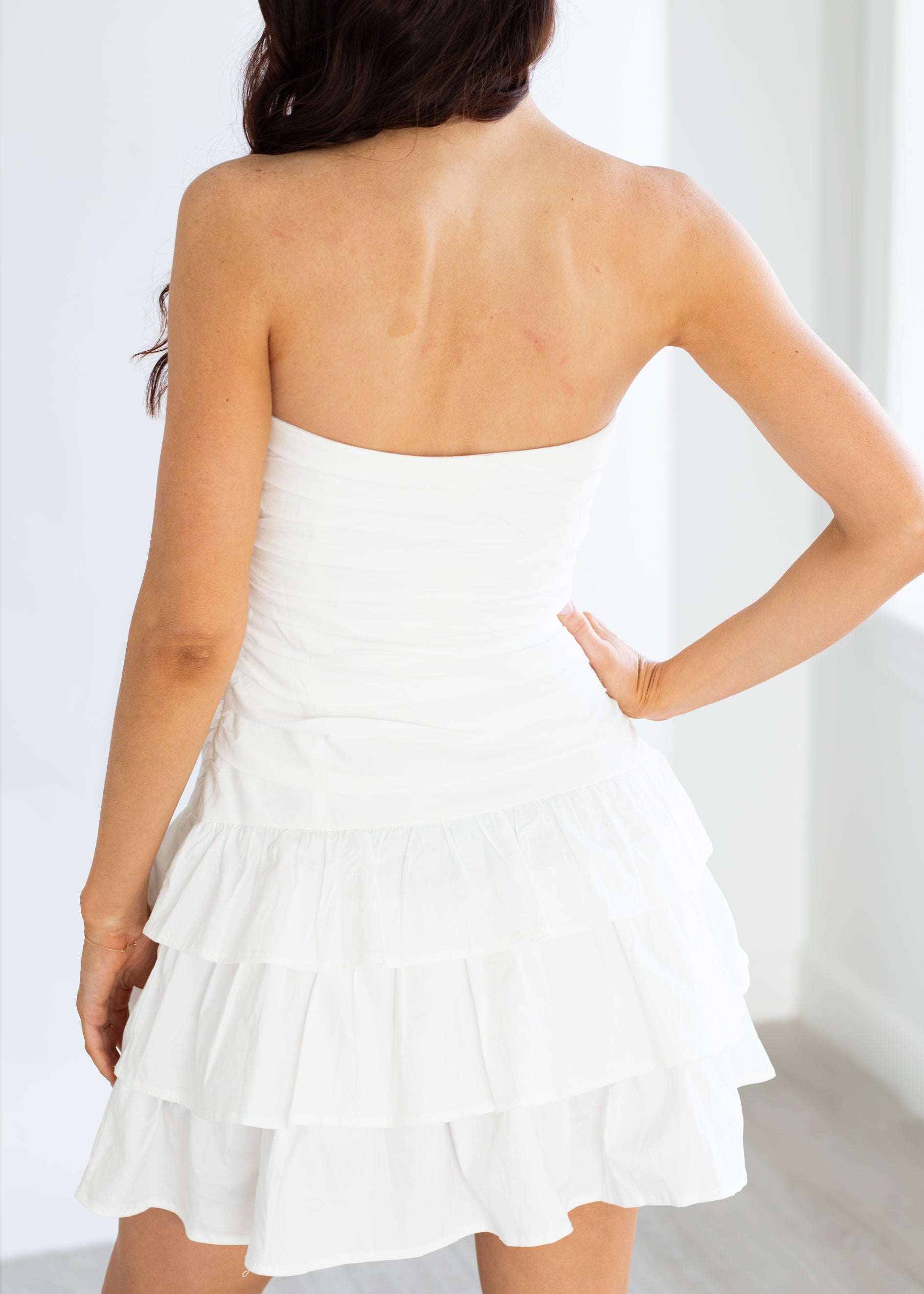 Woman wearing a white strapless dress with ruffled layers against a white background