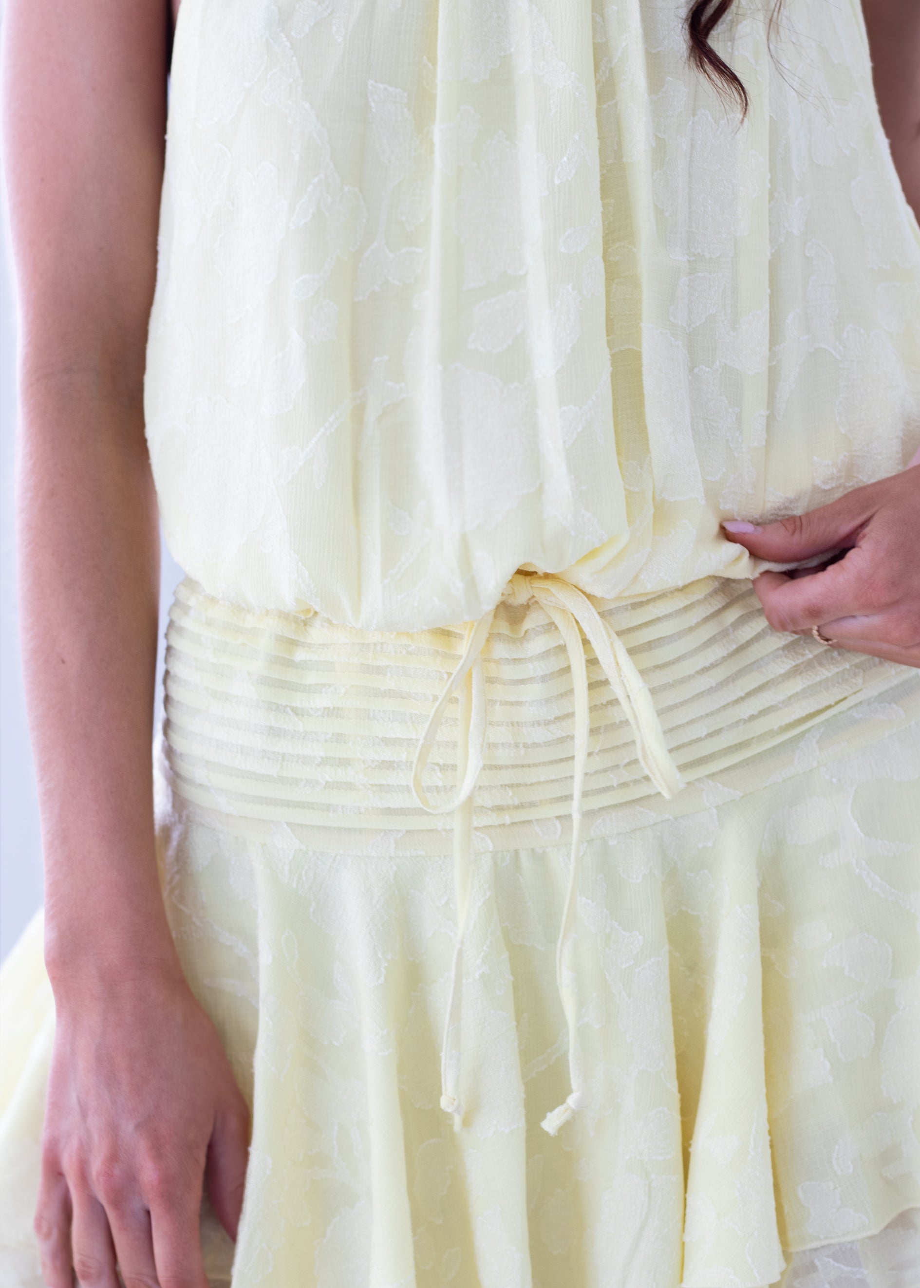 Close-up of a person wearing a light yellow dress with a white background