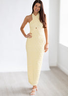 Woman wearing a light yellow halter neck dress against a white background