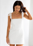 Woman wearing a white dress with sheer sleeves against a white background