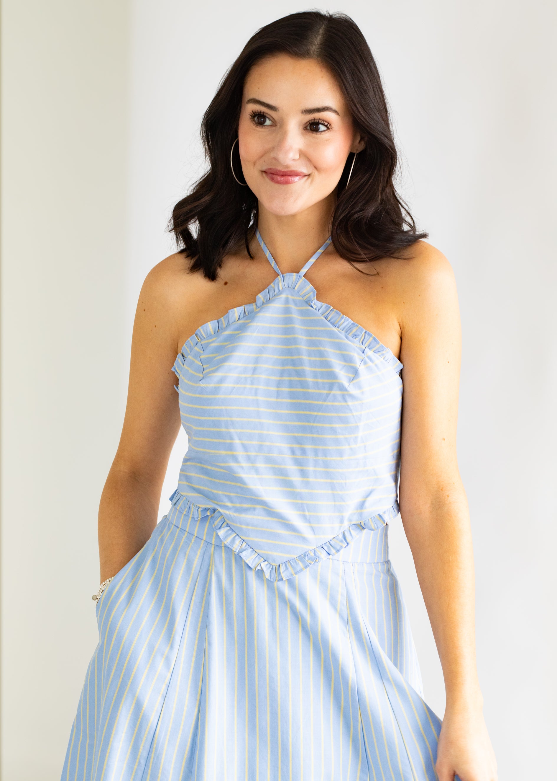 Woman wearing a light blue and white striped dress against a plain background