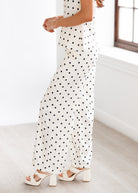 Woman wearing a polka dot dress with white sandals in a minimal indoor setting