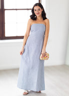 Woman wearing a strapless light blue dress holding a clutch in a minimalistic setting.