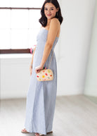 Woman in a light blue dress holding a colorful handbag in a minimalistic setting