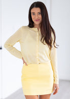 Woman wearing a light yellow skirt standing in a room with a white door.