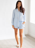 Woman wearing a light blue striped shirt and shorts in a minimal white room.