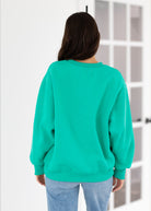 Person wearing a teal sweatshirt in a minimal indoor setting