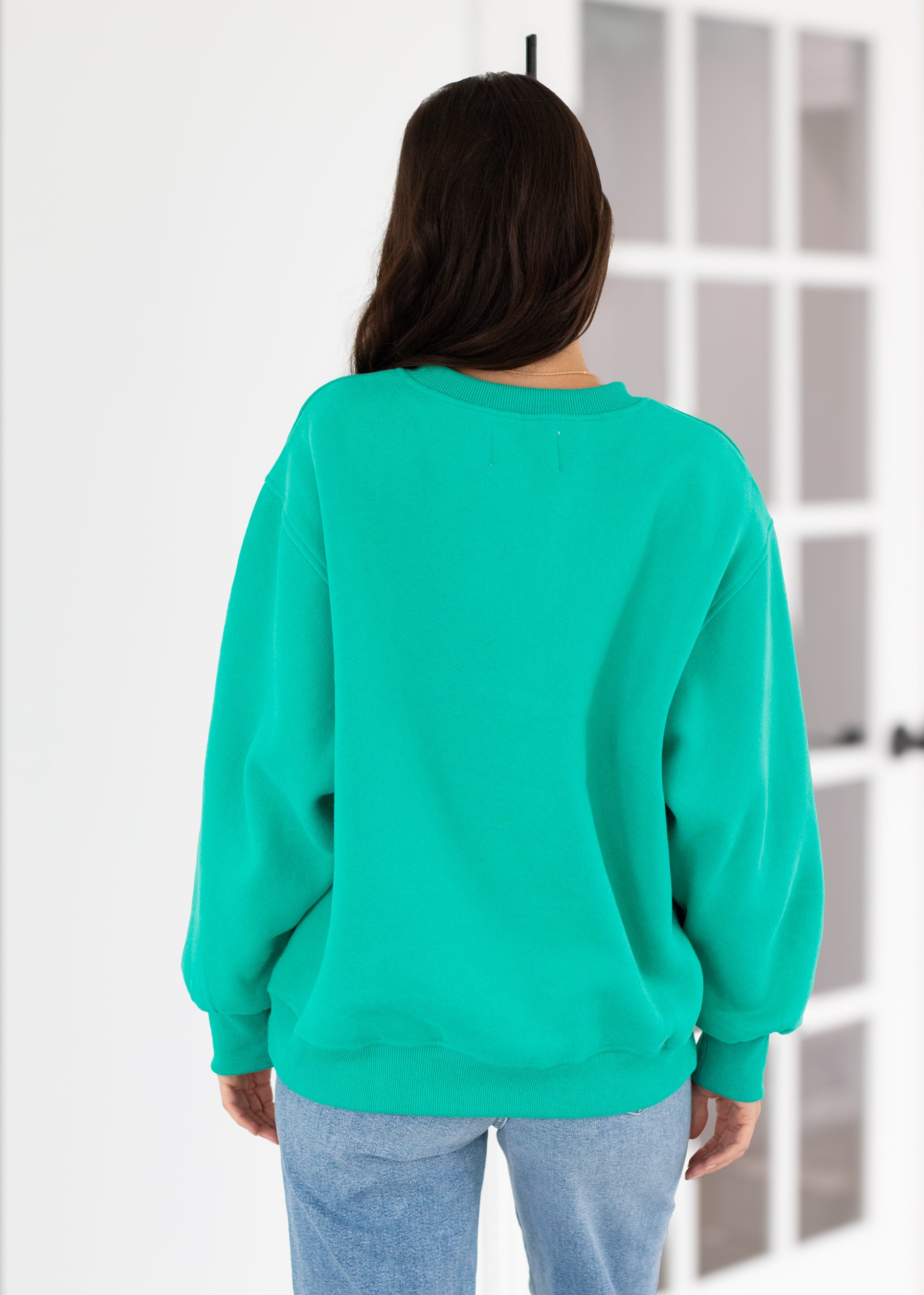 Person wearing a teal sweatshirt in a minimal indoor setting