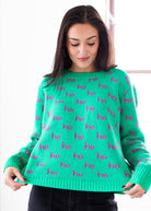 Woman wearing a green sweater with pink 'ho ho ho' pattern on a white background