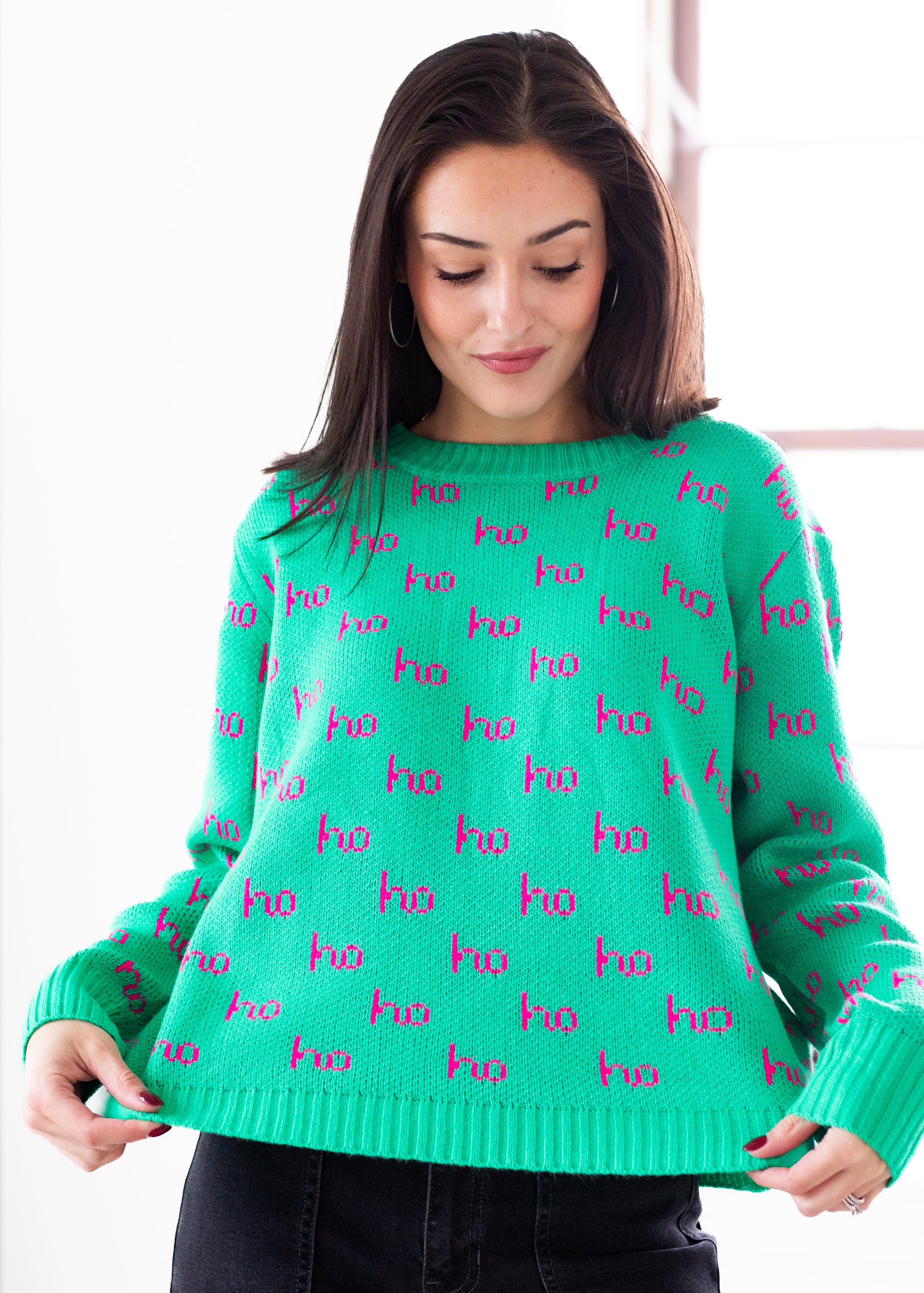 Woman wearing a green sweater with pink 'ho ho ho' pattern on a white background
