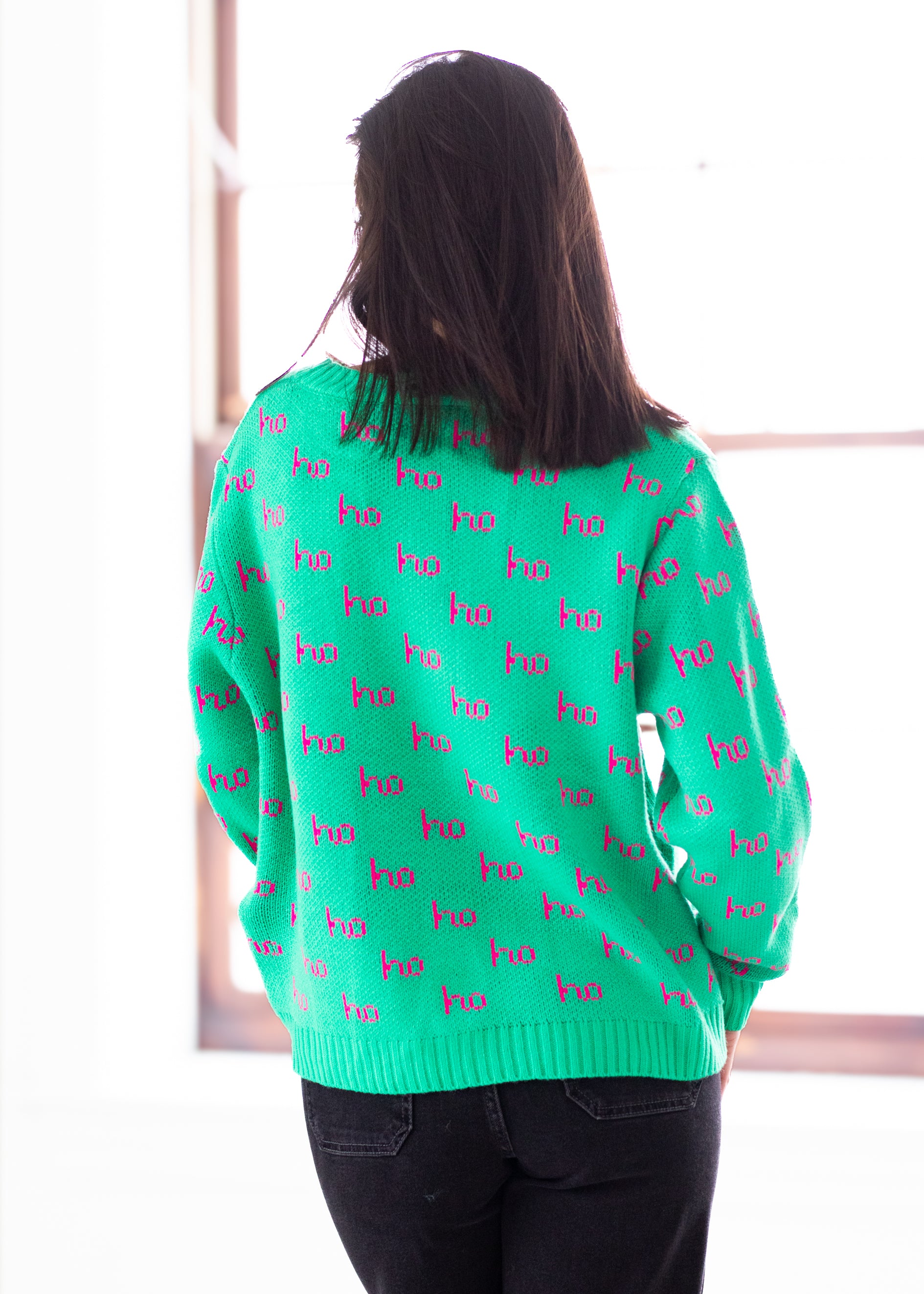 Person wearing a green sweater with pink text, standing against a white background
