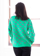 Person wearing a green sweater with pink text, standing against a white background