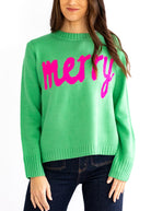 Green sweater with pink 'merry' text worn by a person on a white background