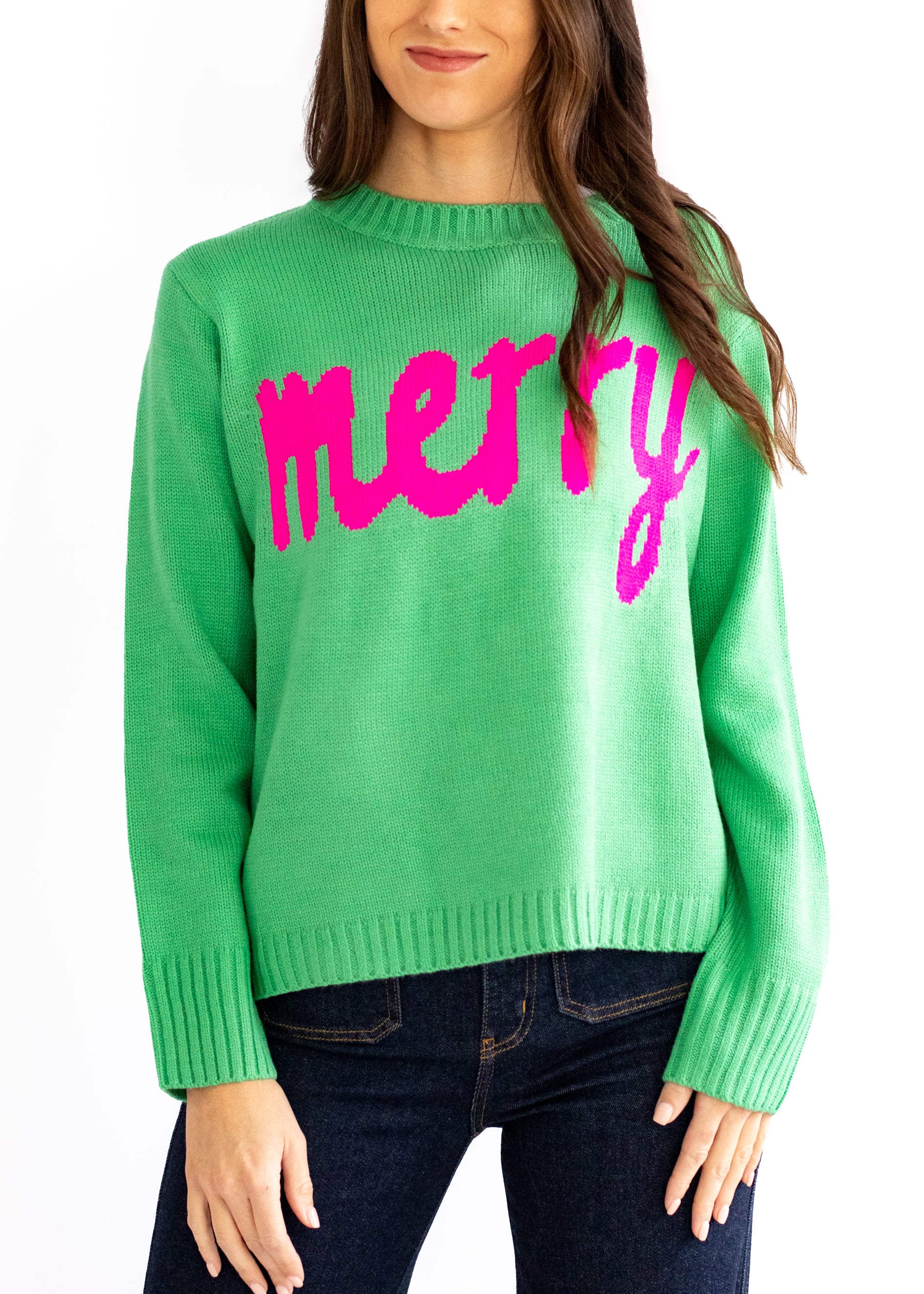 Green sweater with pink 'merry' text worn by a person on a white background