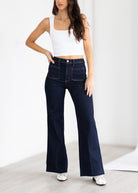 Woman wearing dark blue jeans and a white top on a light background