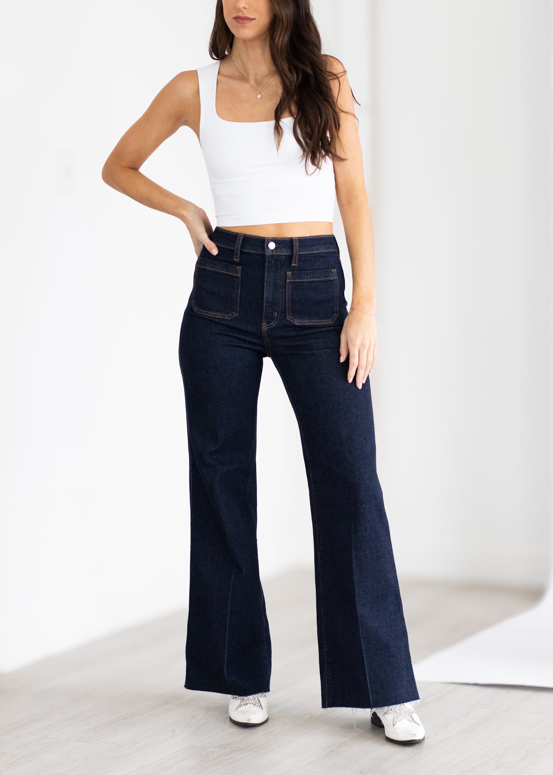 Woman wearing dark blue jeans and a white top on a light background