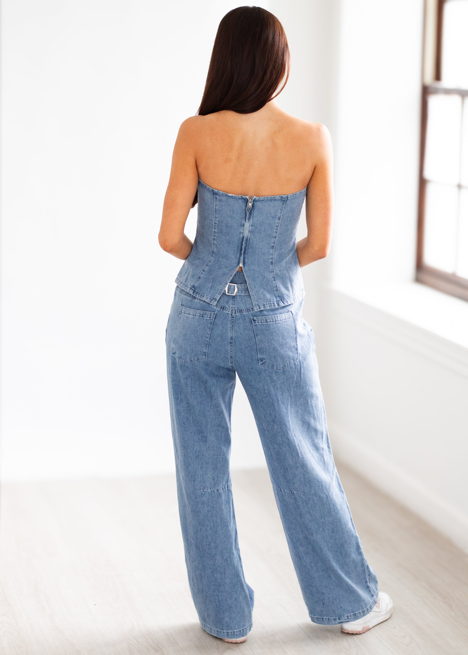 Woman wearing a strapless denim jumpsuit in a minimal indoor setting