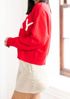 Person wearing a red sweater with a gold logo and a white skirt.