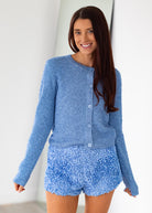 Woman wearing a blue textured cardigan and shorts set against a white background