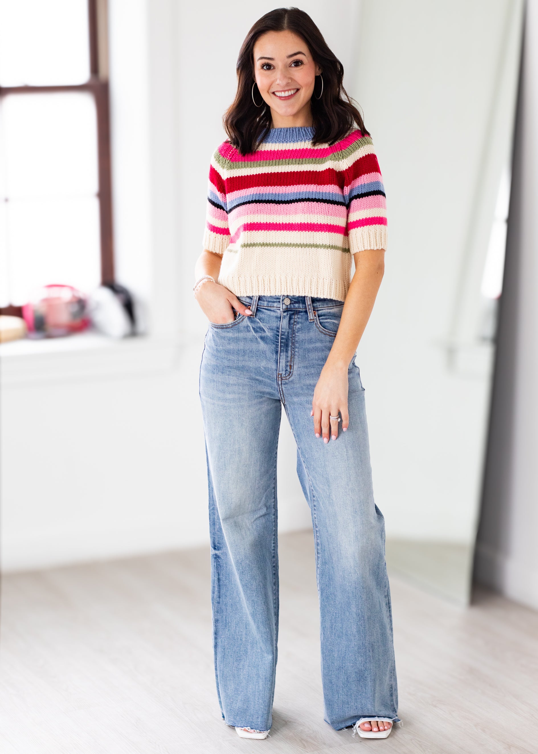 Woman wearing a colorful striped sweater and blue jeans indoors.