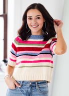 Woman wearing a colorful striped sweater and jeans against a white background