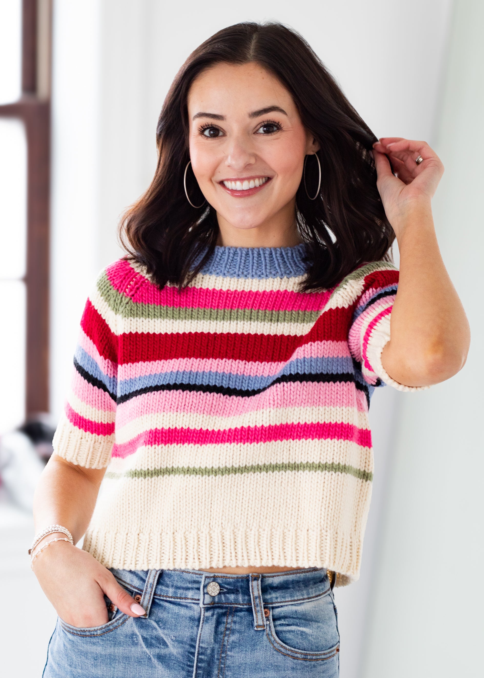Woman wearing a colorful striped sweater and jeans against a white background
