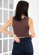 Woman wearing a brown tank top and blue jeans against a white background