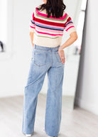 Person wearing a colorful striped sweater and blue jeans indoors.