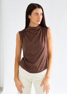 Woman wearing a brown sleeveless top and white pants against a plain background