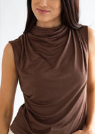 Woman wearing a brown sleeveless top with a draped design on a white background