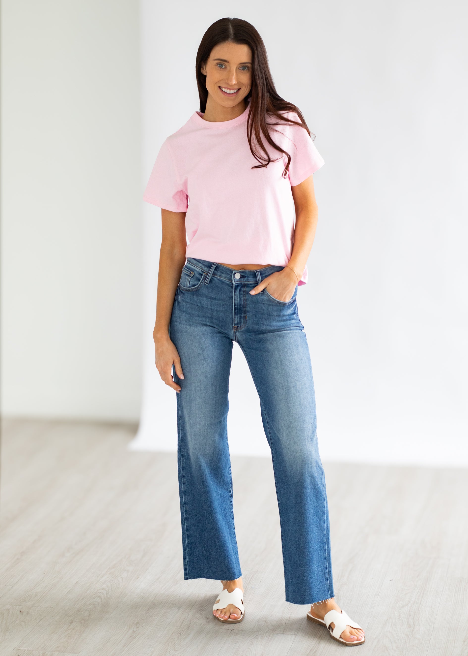 Woman wearing a pink top and blue jeans against a white background