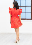Woman wearing a red dress with ruffled sleeves in a minimal indoor setting